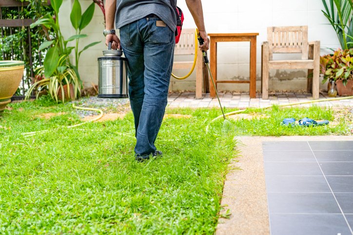 A pest exterminator applies termite control chemicals to a residential yard.