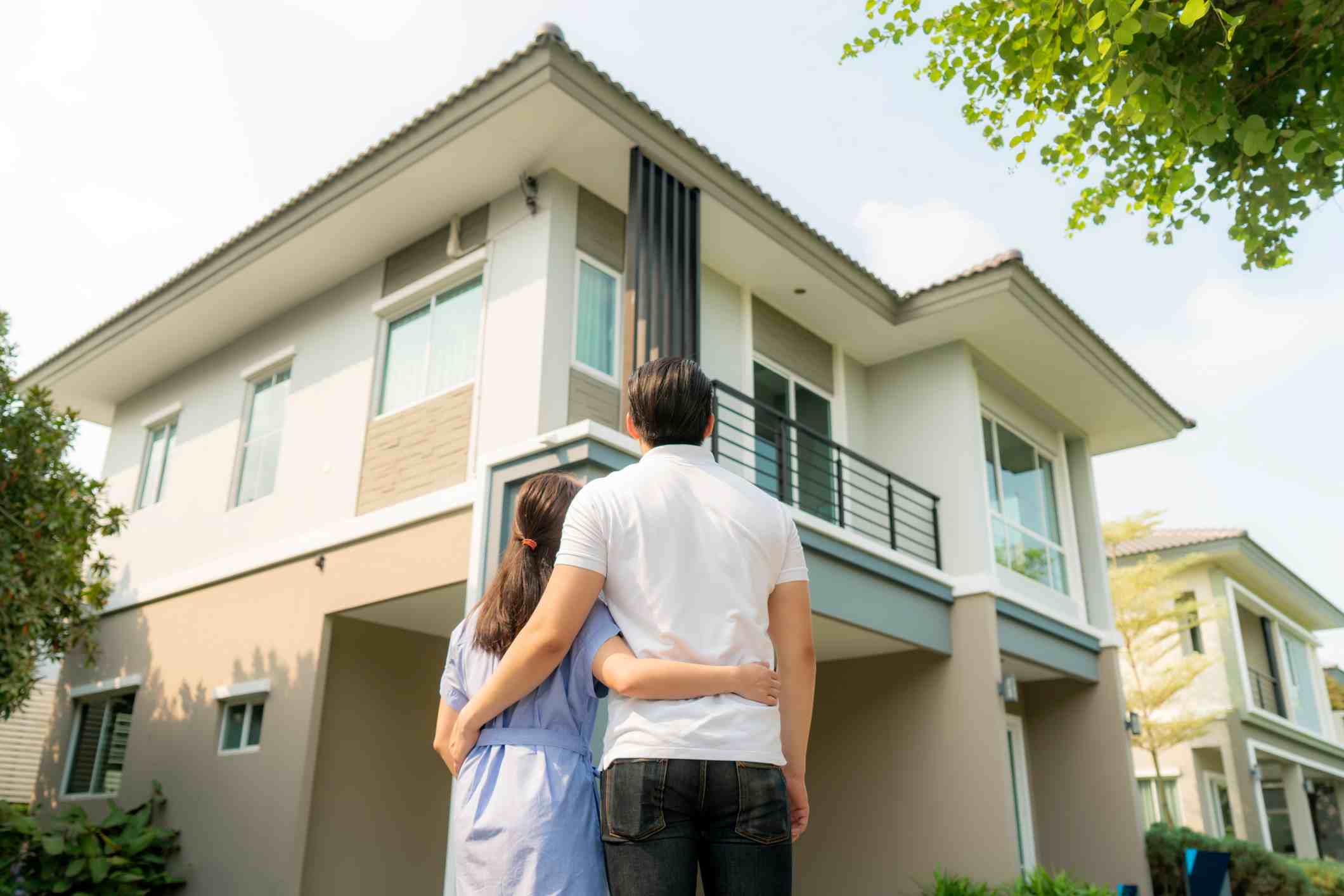 A big white house with modern architectural style, and a couple looking at it while hugging.
